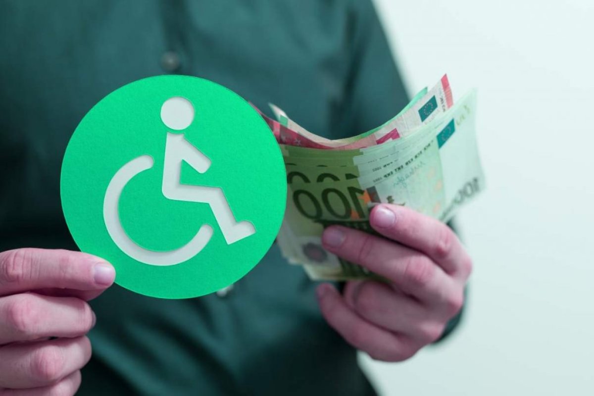 Uomo con in mano un bollino con il simbolo della disabilità e delle banconote euro