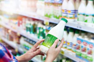 Mani che reggono una bottiglia di latte al supermercato