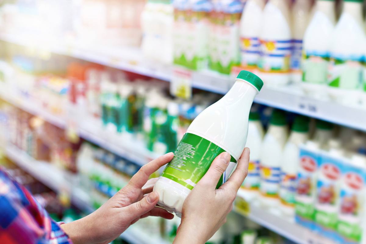 Mani che reggono una bottiglia di latte al supermercato